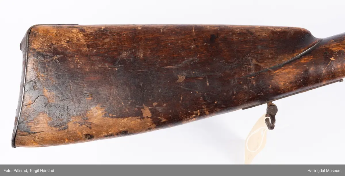 Gevær med perkusjonslås og kassepipe. Har mest sannsynlig vært ombygd fra flintlås. Geværet har kassepipe - har firkantet løp bakerst fra låsen til siktet midt på løpet. Fra låsen til siktet midt på løpet er løpet kasseformet og har en dekorert overgang til et svakt avrundet åttekantet løp. Det fremste siktet er av messing. Kolbekappen er festet med to skruer. Mangler avtrekksbøyle, reim og ladestokk. Montert på patentsvansskrue ved ombygging. Løpet er 15 cm i diameter og glattløpet.