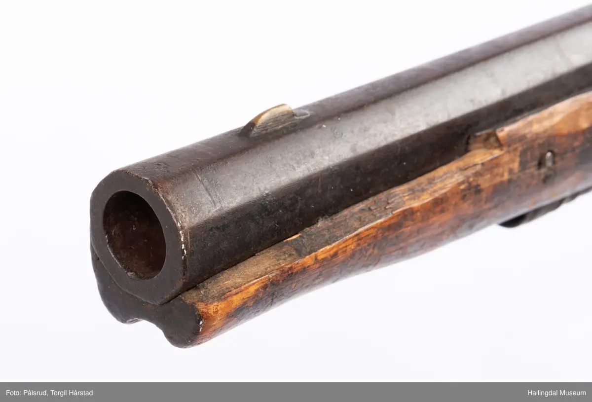 Gevær med perkusjonslås og kassepipe. Har mest sannsynlig vært ombygd fra flintlås. Geværet har kassepipe - har firkantet løp bakerst fra låsen til siktet midt på løpet. Fra låsen til siktet midt på løpet er løpet kasseformet og har en dekorert overgang til et svakt avrundet åttekantet løp. Det fremste siktet er av messing. Kolbekappen er festet med to skruer. Mangler avtrekksbøyle, reim og ladestokk. Montert på patentsvansskrue ved ombygging. Løpet er 15 cm i diameter og glattløpet.