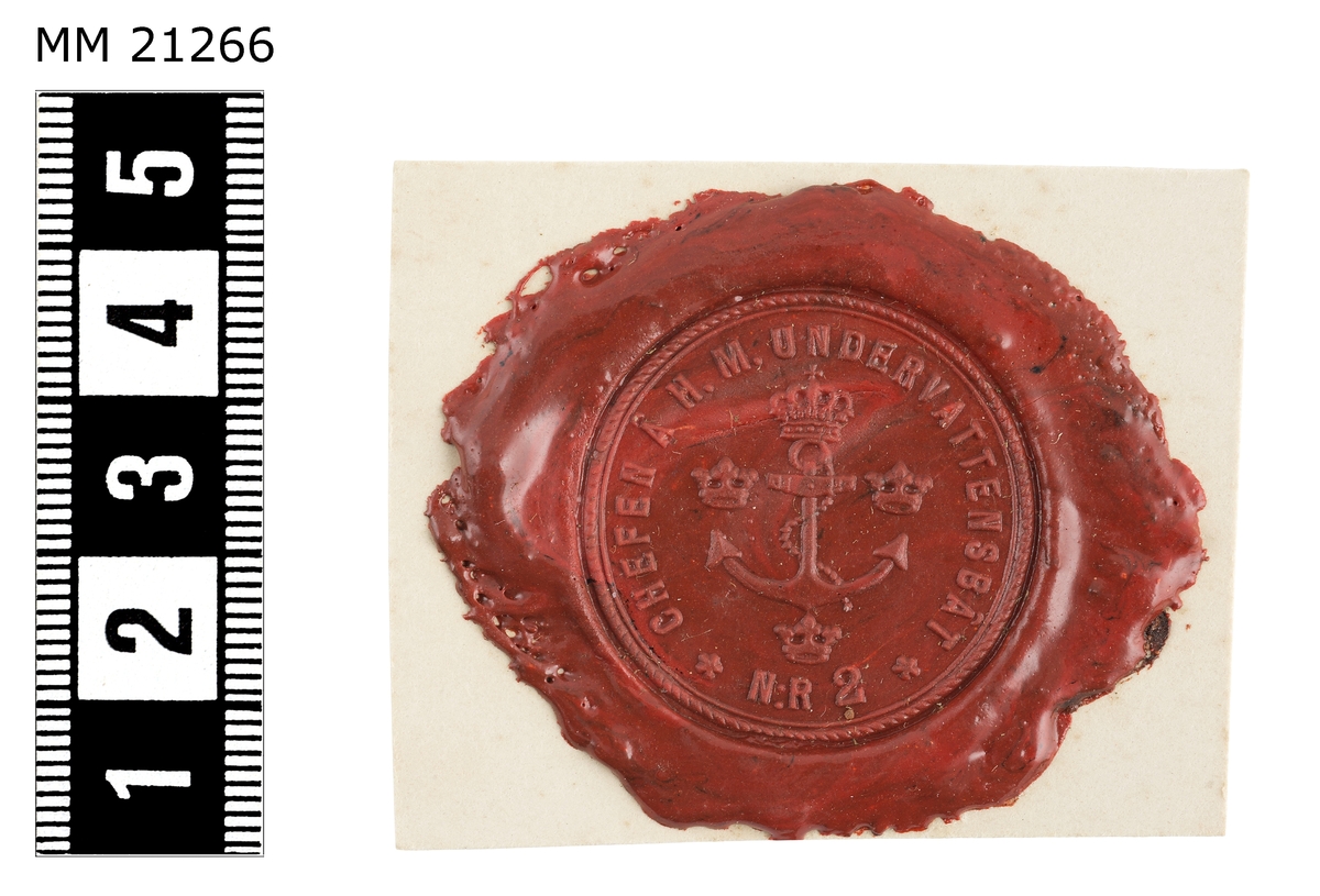 Sigillavtryck av rött lack på papper. I mitten krönt stockankare omgivet av tre kronor. Längs kanten text: "Chefen å H.M. undervattensbåt Nr 2".