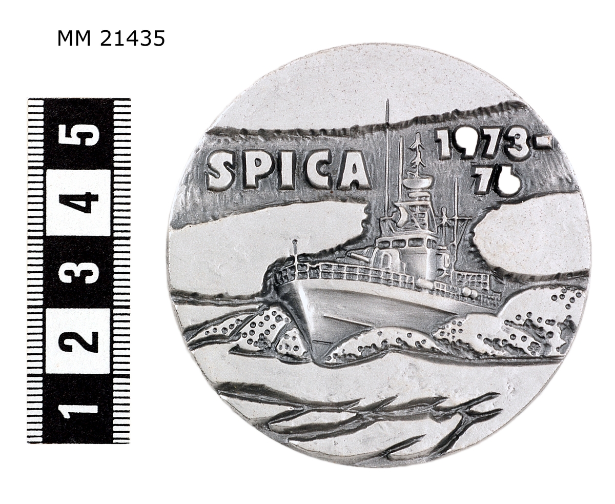 Minnespenning  av vitmetall, kraftig med djup dekor, utan kant. Åtsida: Spica på sjön med fören mot bildytan. Markerade moln. Överst text: "SPICA 1973-76". Frånsida: ruta med infälld text: samtliga robotbåtar av Norrköpingklass samt längs kanten: "BYGGDA VID KARLSKRONAVARVET AB"

På kanten "SPORRONG".