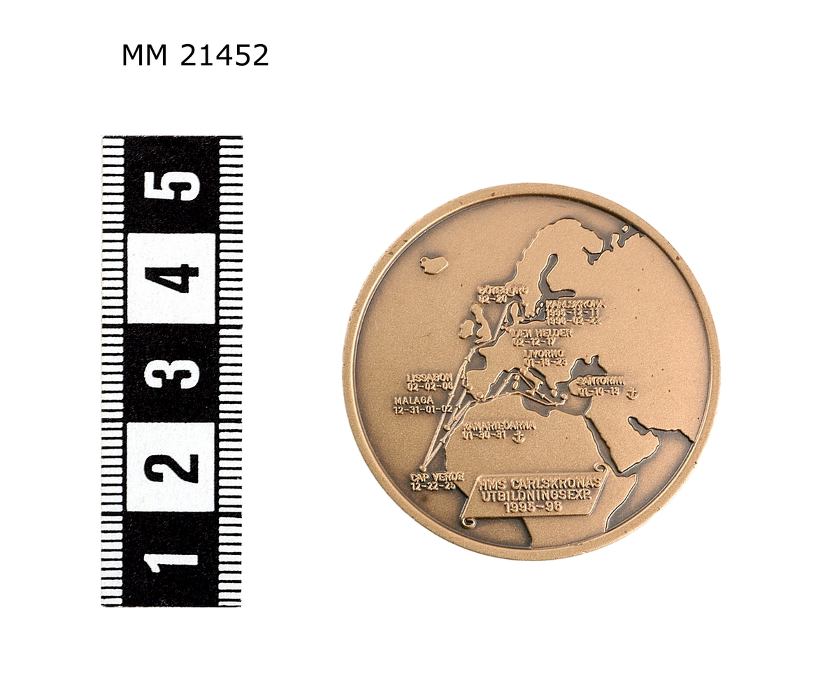 Minnespenning av brons. Åtsida: Fartyg på sjön visande babordssidan. Nedanför krönt stockankare. Runt kant text: "HMS CARLSKRONA". Frånsida: Karta visande Europa samt delar av Afrika och Asien med hamnarnas namn. Banderoll med text: "HMS CARLSKRONA LÅNGRESAN 1995-96". Kant runt om.