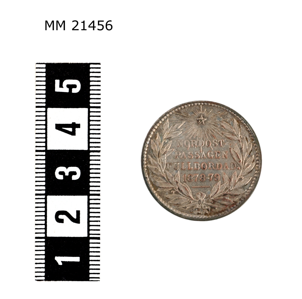 Minnespenning av silverplätering. Åtsida: Huvud i profil av man med mustasch. Under bild text : "LINDBERG". Längs kanten text: "ADOLF ERIK NORDENSKIÖLD". Prickad rand längs kanten.

Frånsida Lagerkrans runt kanten, överst strålande stjärna, text i mitten: "NORDOSTPASSAGEN FULLBORDAD 1878-79".