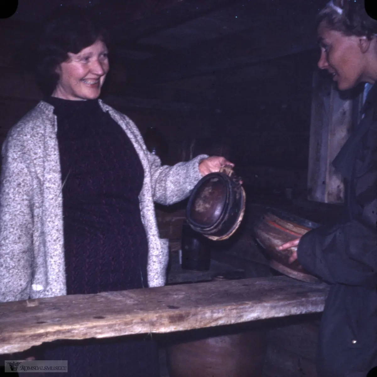 Brennevinsbua, Fiskerimuseet. Anne Strømme f. Ræstad 27.01.1918 d.03.07.2009. viser fram ein brennevinskagge. Ho var vertskap på Fiskerimuseet nokre somrar mellom Erling og Emilie Lyngvær og Leonard og Olette Rasmussen.