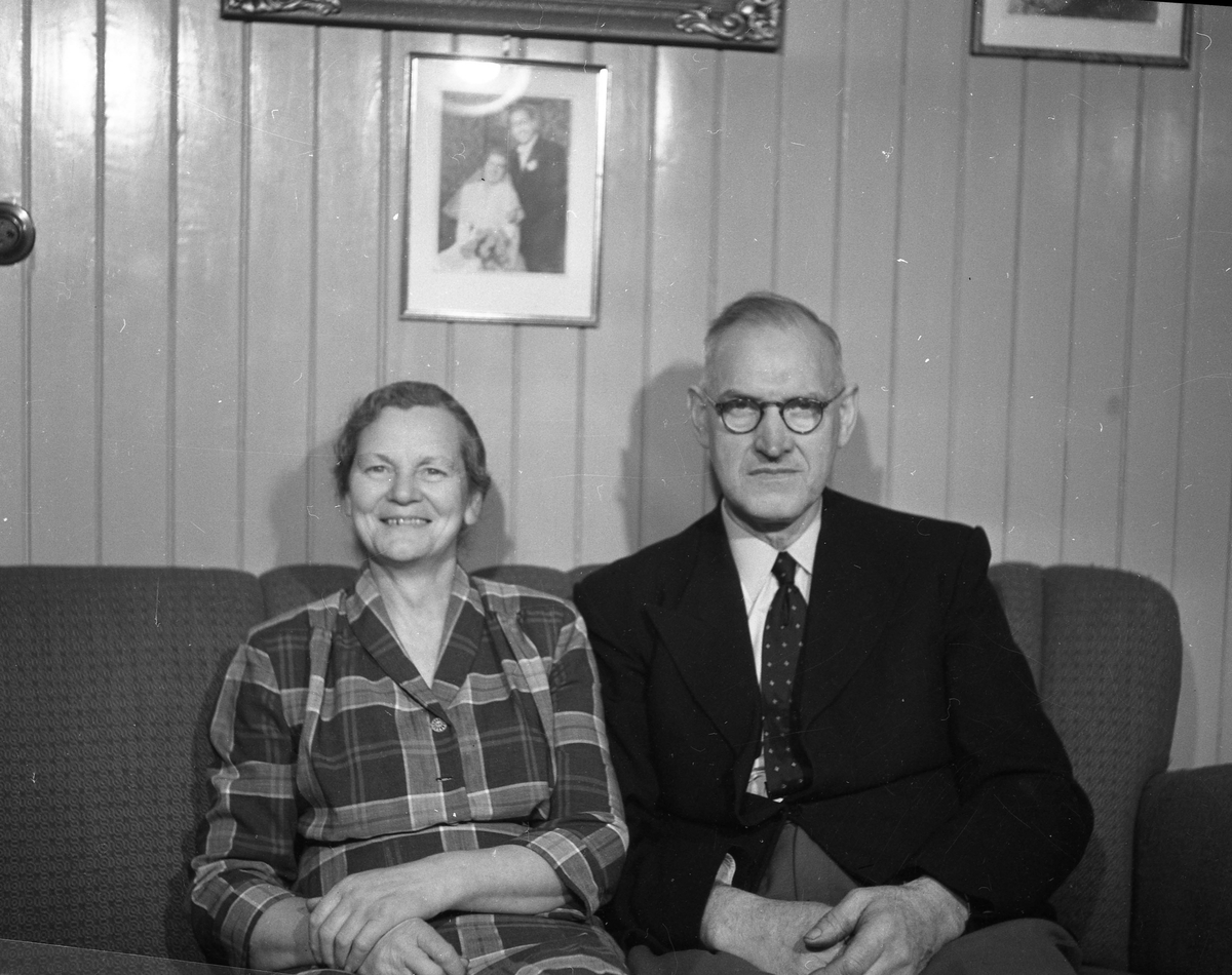 Et par sittende i sofa. Brudebilde på veggen over dem.