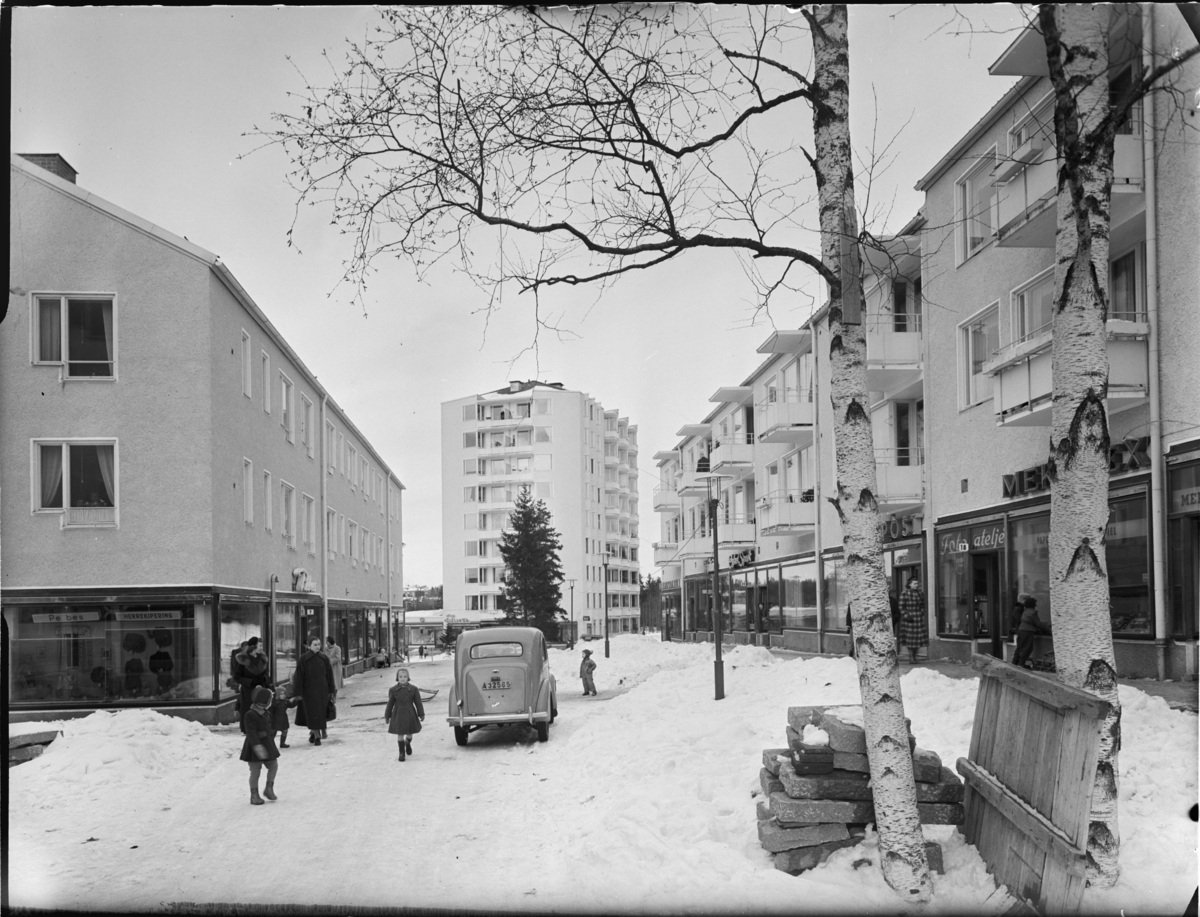 Hökarängens centrum
Exteriör, i bakgrunden, flerbostadshus med butiker i förgrunden. Barn, bilar, vinter.