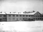 Tvåvånings fabriksbyggnad i trä. Gårdsidan.
Bilden tagen från Olaigatan. Två bussar, AB Mellansvensk Omnibusstrafik.
Fabrikör Johan Behrn