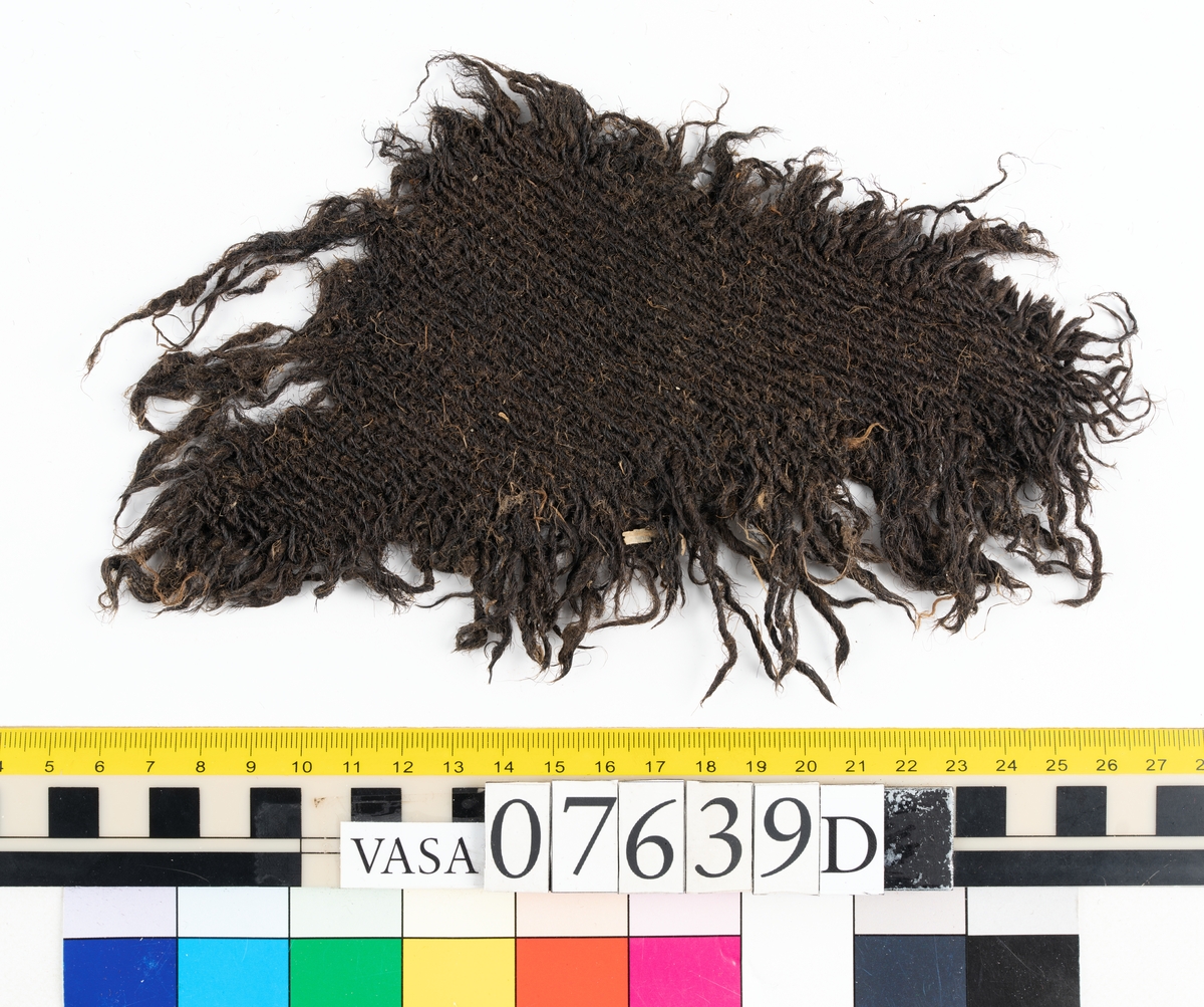 Textilfragment. 53 fragment fördelade på fyndnummer 07639a-e.
Fnr 07639a består av 17 fragment av ull vävda i tuskaft.
Fnr 07639b består av 8 fragment av hattfilt.
Fnr 07639c består av 17 fragment av ull vävda i kypert.
Fnr 07639d består av 1 fragment av ull vävt i kypert.
Fnr 07639e har 10 fragment av ull vävda i tuskaft varav ett fragment har en stadkant.

Textildokumentation 2017:
07639b
9 fragment i hårt filtad filt. Filten är tjock och kompakt, typ 1:1 har även en klippt eller skuren del. Sidan ett (synlig på bilden 1) är mycket mörkare i ytan, nästan svart, medan sida två går mer åt brunt. Båda sidorna har synliga märken efter avtryck, På sida två syns dessa bäst. En del hår i filten är finare än andra och dessa blänker mer. Möjligen är materialet bäver.
07639d:
Ett tygfragment i kompakt, tät och grov kypert, typ 3:1. Fragmentet har kraftigt upprepade kanter runtom. Tjocka fransar har bildats på den längsta sidan, dessa består av trådsystem 1. Trådsystem 1 är mycket hårt Z-tvinnat, nästan så att det lägger sig i öglor. Tyget är glansigt och på sida ett ser det något ripsartat ut, då trådsystem 1 nästan inte syns, utan bara randningen.  Sida två av tyget har nötningar och glesare kypertränder.