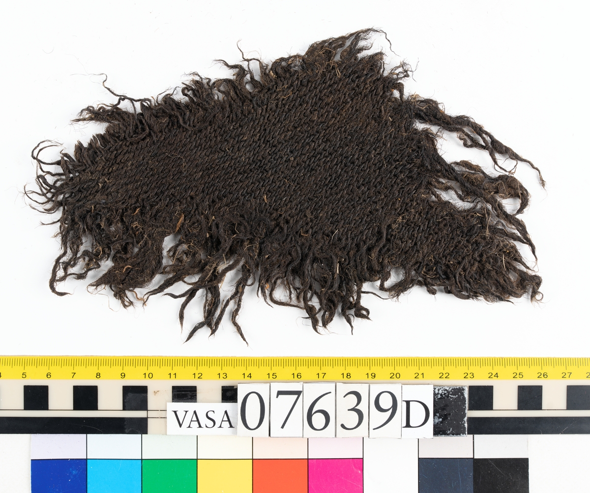 Textilfragment. 53 fragment fördelade på fyndnummer 07639a-e.
Fnr 07639a består av 17 fragment av ull vävda i tuskaft.
Fnr 07639b består av 8 fragment av hattfilt.
Fnr 07639c består av 17 fragment av ull vävda i kypert.
Fnr 07639d består av 1 fragment av ull vävt i kypert.
Fnr 07639e har 10 fragment av ull vävda i tuskaft varav ett fragment har en stadkant.

Textildokumentation 2017:
07639b
9 fragment i hårt filtad filt. Filten är tjock och kompakt, typ 1:1 har även en klippt eller skuren del. Sidan ett (synlig på bilden 1) är mycket mörkare i ytan, nästan svart, medan sida två går mer åt brunt. Båda sidorna har synliga märken efter avtryck, På sida två syns dessa bäst. En del hår i filten är finare än andra och dessa blänker mer. Möjligen är materialet bäver.
07639d:
Ett tygfragment i kompakt, tät och grov kypert, typ 3:1. Fragmentet har kraftigt upprepade kanter runtom. Tjocka fransar har bildats på den längsta sidan, dessa består av trådsystem 1. Trådsystem 1 är mycket hårt Z-tvinnat, nästan så att det lägger sig i öglor. Tyget är glansigt och på sida ett ser det något ripsartat ut, då trådsystem 1 nästan inte syns, utan bara randningen.  Sida två av tyget har nötningar och glesare kypertränder.