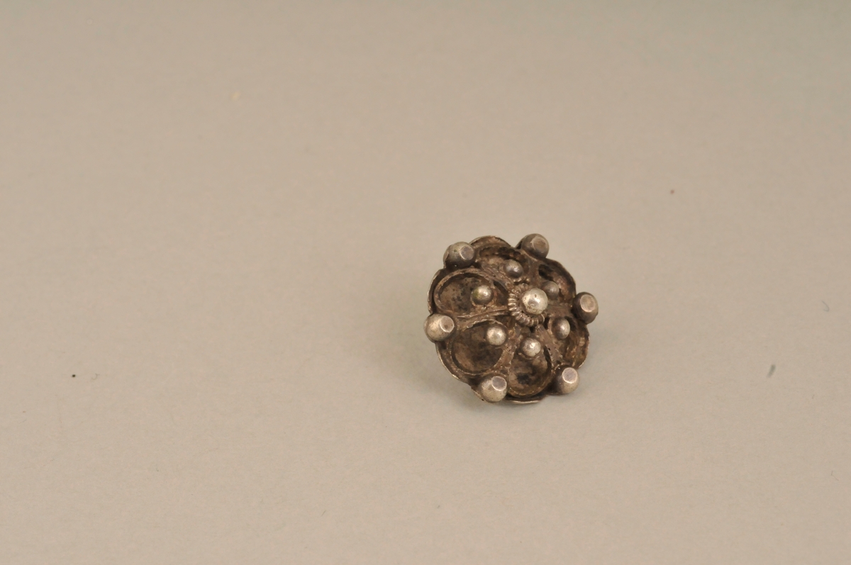 Høg knapp med flat filigransrose på toppen, pålodda hempe. Sylvstempel.