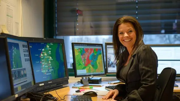 Foto av kvinne som sitter ved skrivebord med mange pc-skjermer