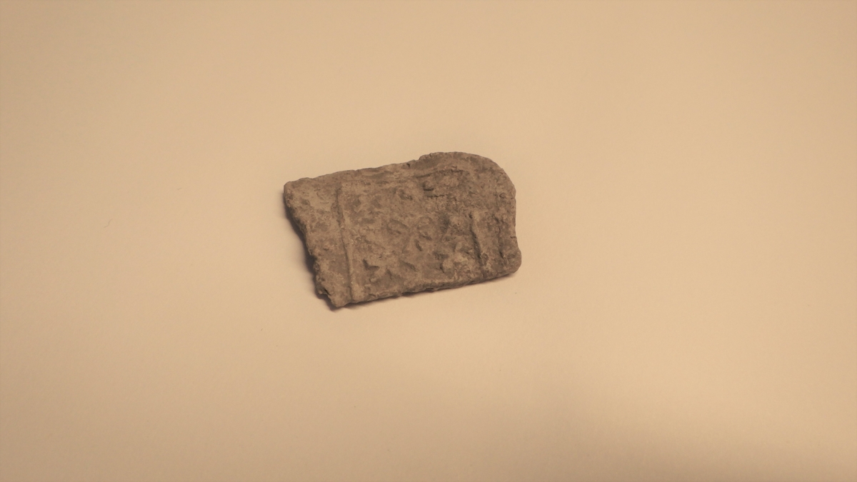 Uregelmessig metallplate med dekor innenfor et avgrenset kvadratisk felt. Dekoren har en åttearmet stjerne i midten.