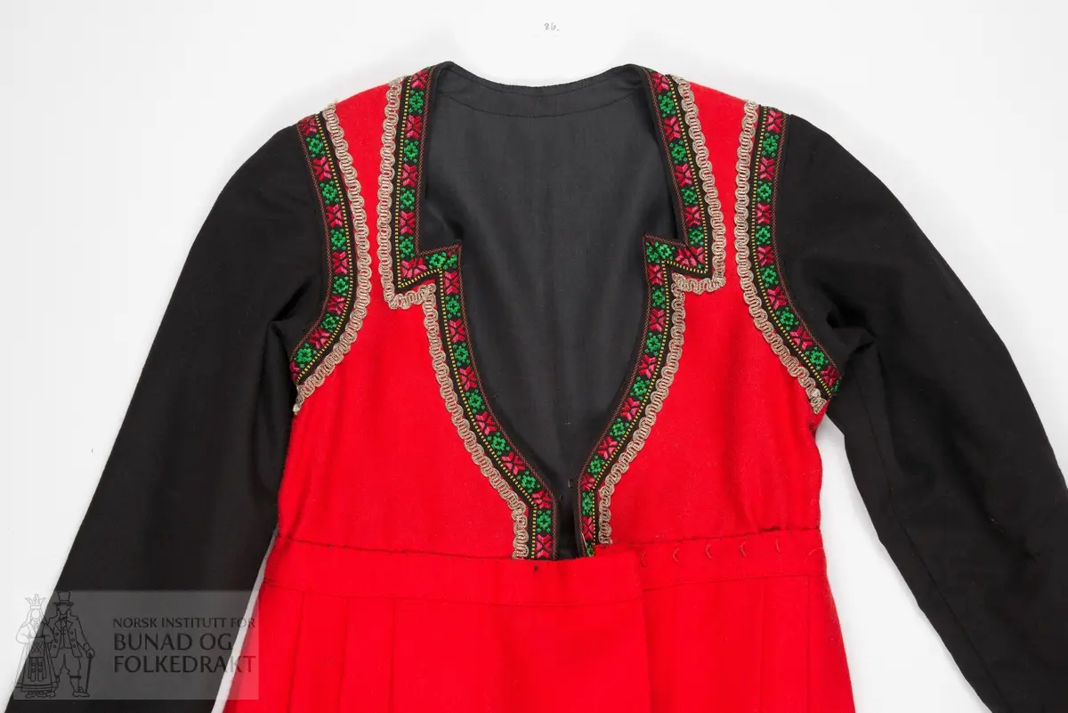 Kjole.
Trøye sydd til stakk. Trøya har røde forstykker, det er ikke en hel trøye som har fått røde fremstykker/bringesylv sydd på utenpå. 
Det svarte stoffet er et tynt ullstoff, det røde er litt kraftigere, begge er i lerretsbinding.
Foret med svart bomullslerret. Kanta med svarte bomullsbånd med blomstermønster, samt sølvfargede metallbånd.
Lukkes midt foran med hekter. 
Stakken er av rød ull, samme type som i livet. Lagt i legg til linningen med et flatt parti foran. 
Splitt midt foran, linningen lukkes med hekter. Stakken er uforet. Kanta nederst med en bred bord av samme svarte ullstoff som i trøya, stakkekanten er i tillegg dekorert med to rader sølvfargede metallbånd, samme type som på trøya. 
Både håndsøm og maskinsøm.