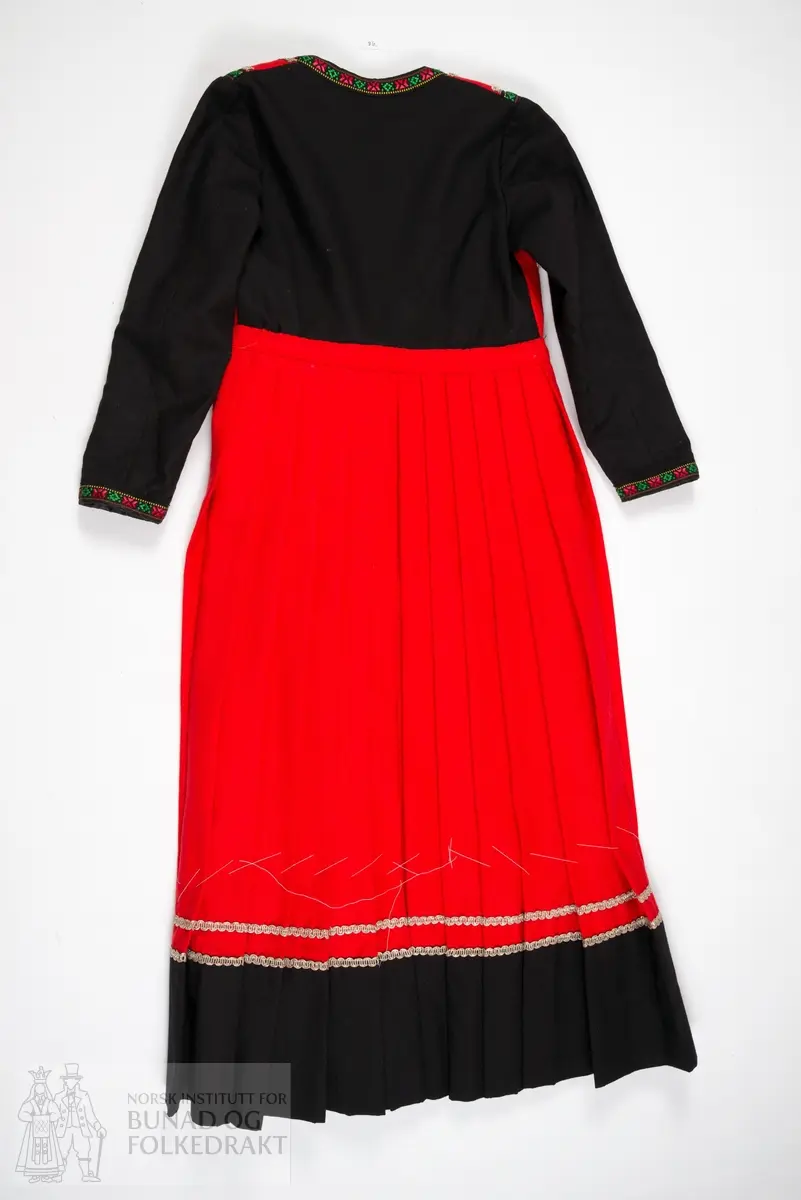 Kjole.
Trøye sydd til stakk. Trøya har røde forstykker, det er ikke en hel trøye som har fått røde fremstykker/bringesylv sydd på utenpå. 
Det svarte stoffet er et tynt ullstoff, det røde er litt kraftigere, begge er i lerretsbinding.
Foret med svart bomullslerret. Kanta med svarte bomullsbånd med blomstermønster, samt sølvfargede metallbånd.
Lukkes midt foran med hekter. 
Stakken er av rød ull, samme type som i livet. Lagt i legg til linningen med et flatt parti foran. 
Splitt midt foran, linningen lukkes med hekter. Stakken er uforet. Kanta nederst med en bred bord av samme svarte ullstoff som i trøya, stakkekanten er i tillegg dekorert med to rader sølvfargede metallbånd, samme type som på trøya. 
Både håndsøm og maskinsøm.