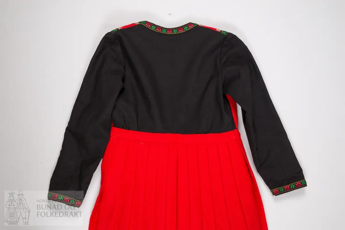 Kjole.
Trøye sydd til stakk. Trøya har røde forstykker, det er ikke en hel trøye som har fått røde fremstykker/bringesylv sydd på utenpå. 
Det svarte stoffet er et tynt ullstoff, det røde er litt kraftigere, begge er i lerretsbinding.
Foret med svart bomullslerret. Kanta med svarte bomullsbånd med blomstermønster, samt sølvfargede metallbånd.
Lukkes midt foran med hekter. 
Stakken er av rød ull, samme type som i livet. Lagt i legg til linningen med et flatt parti foran. 
Splitt midt foran, linningen lukkes med hekter. Stakken er uforet. Kanta nederst med en bred bord av samme svarte ullstoff som i trøya, stakkekanten er i tillegg dekorert med to rader sølvfargede metallbånd, samme type som på trøya. 
Både håndsøm og maskinsøm.