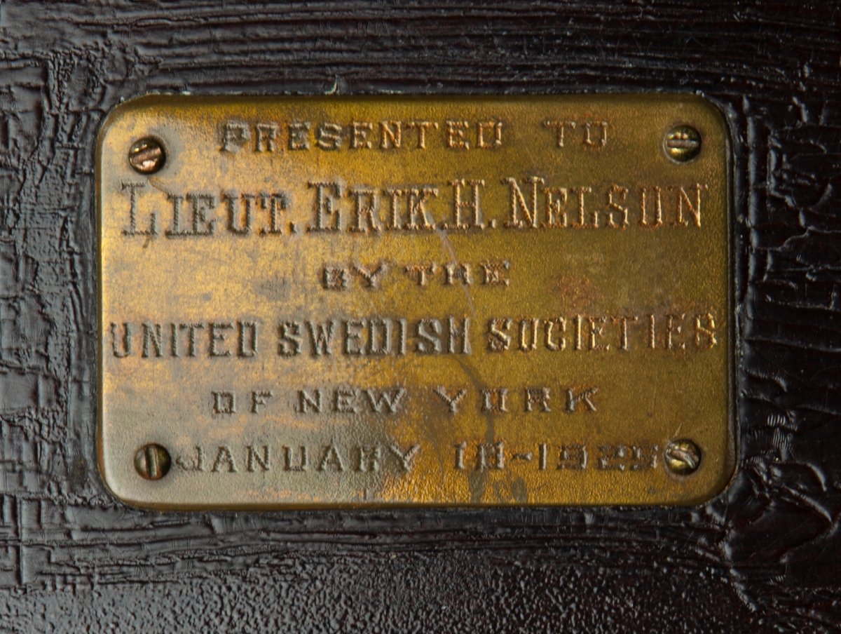 Matsilver i shatull tillverkad av International Silver Co. 
Besticken förvaras i ett träschatull klätt invändigt med sammet. Text på locket: "Presented to Lieut. Erik H Nelson by the United Swedish societs of New York. January 1925". 
Det översta facket innehåller: 12 teskedar, 12 soppskedar och 6 matskedar. Nedre facket: 12 matknivar med blad av rostfritt stål och skaft av silver samt 12 matgafflar. Alla delarna med märkt med N. I schatullet ligger en nyckel till låset samt ett kuvert med anteckning på innehåll.