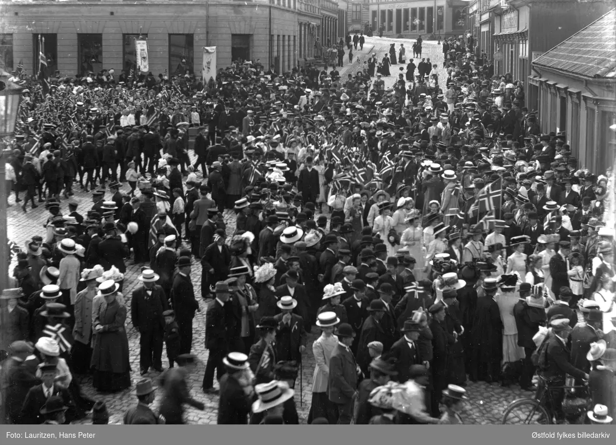 17 mai tog i Moss 1911. Kongens gate i Moss med Torget på venstre side,  Hjørnegården til venstre er nr. 26 (idag Moss Stentøymagasin, Grenness eft.). Til høyre hjørnegården - Henrik I. Larsen A/S. Rett etter dette er porten inn til skredderforr. O. M. Olsen hvor ant. fotografen H. P. Lauritzen gikk i lære. Så L. P. Sterud og i svingen Rygge Sparebank.