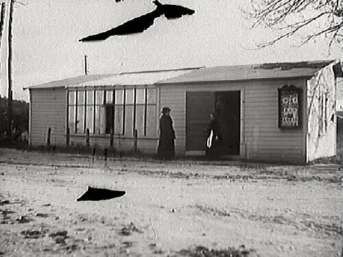 Exteriör av fotoateljén som fotograf Mathilda Ranch lät uppföra som filial på Stationsgatan i Slöinge vid 1890-talets mitt. Till höger på fasaden sitter ett skyltskåp med fotografier som ska göra reklam för ateljén, som endast var öppen sommartid. Sedan 1894 hade hon haft en ateljé inrymd i Villa Fridhem, ägd av Sven Christiansson. Sven blev föreståndare för filialen och gifte sig med Mathildas piga Anna år 1899. Annas mor Kristina Dahl var hushållerska åt Sven. I bild finns telefon- respektive elstolpar. (Skador på negativet ger stora svarta fläckar)