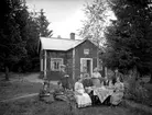 Bostadshus, släktgrupp 9 personer framför huset.
Knut Albin Blyckerts 70 årsdag. Han är född 1864.
Med på bilden bl.a. Carolina Mathilda Schöllin (Sam Lindskogs moster Tilda), Sam Lindskog och hans hustru Hulda Lindskog.
Mannen längst till höger är Tildas och Knut Albins son, Sven Blüchert. Kvinnan stående i mitten är Stina Blüchert, Sven Blücherts dotter.
Mannen sittande till höger på bilden kan vara Oskar Johansson (Tildas son) och kvinnan sittande till höger kan vara Oskars fru.
Kvinnan längst till vänster är troligen Selma (gift Andersson), Sam Lindskogs syster.