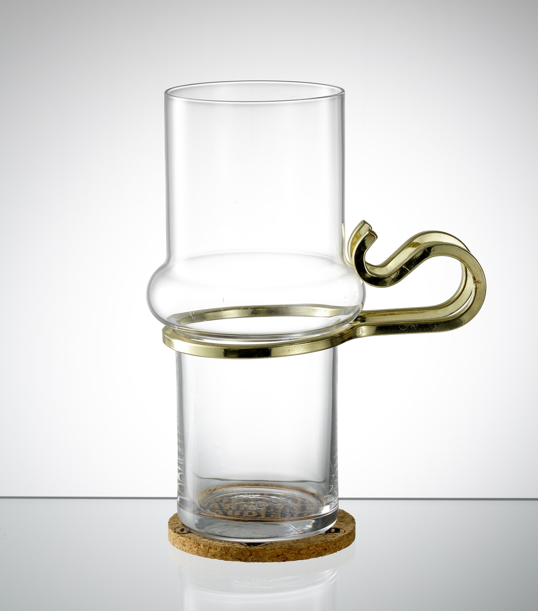 "Varm Kall", formgiven av Lindau & Lindekrantz. Cylindrisk form med vulst på kupans mittdel. Öra i mässing. Tillhörande underlägg i kork.