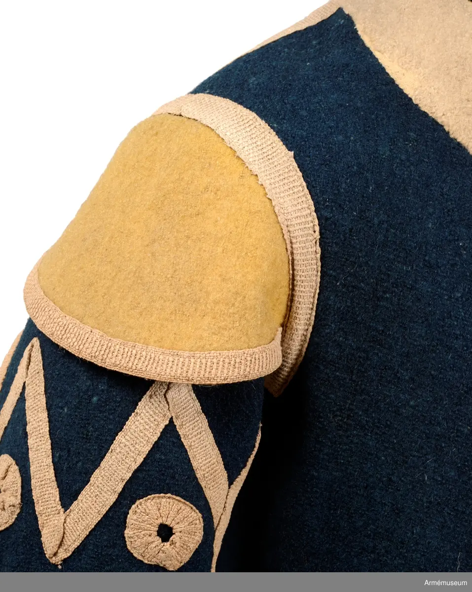 Rock av blått kläde med vita ärmuppslag och bröstrevärer av vitt kläde, gula axelkarmar, dekorationer av vävda vita band i tre olika bredder och släta mässingsknappar. Rocken är lång, med svängd mitt-fram-linje. Troligen nådde den nästan till knät på den som bar den. Den har 20 parvis ställda knappar fram, men knäpps kant i kant med två hyskor och hakar.
Den är konstruerad med hela framstycken som går runt till baksidan och bildar sidstycken. Delat bakstycke med mitt-bak-söm, samt tvåsömsärm. Sidsömmarna, ärmsömmarna och mitt-bak-sömmen är dekorerade med band. Två lågt ställda horisontella fickor fram med bandprydda ficklock, falska knapphål och två knappar vardera.
Skört med uppvik nertill fram. Sicksackdekorationer och rundlar på ärmarna.
Foder av vit boj i bålen, men oblekt bomull i ärmarna.