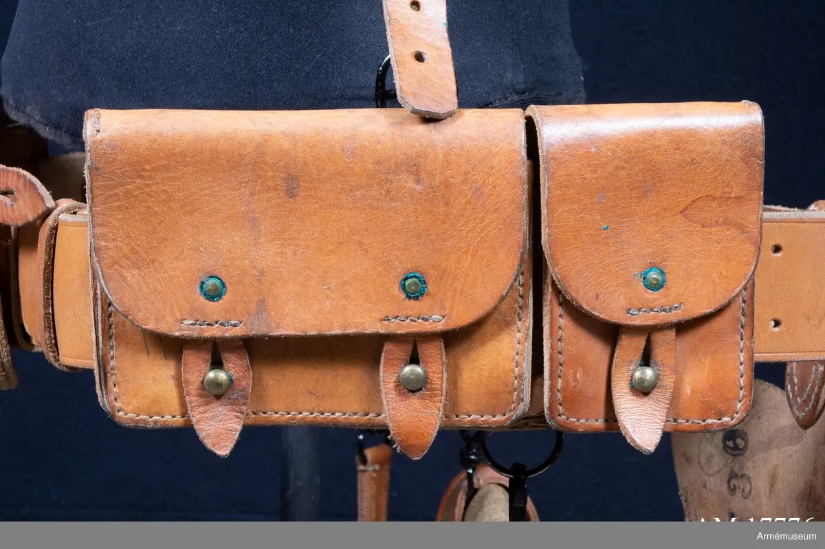 Grupp C I.
Ammunitionsväska, större. Av brunt läder, naturfärg. På framsidan två knappar. Locket har två läderbitar med knapphål.

Ur uniform m/1936 för menig vid 153:e infanteriet, Frankrike. M/1936 enl uppgift från M Boulin. Består av rock, skjorta, slips, byxa, benlindor, kängor, hjälm, kappa, livrem, ammunitionsväskor, tornistrar, ränsel, vin- flaska.