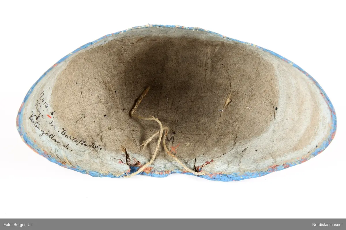 Huvudliggaren bilaga= "Två hvardagsmössor" från Härja socken i Vestergötland, såsom de allmänt begagnades på 1830-talet af gifta qvinnor."

a. Bindmössa, mått från öra till öra 35 cm, djup 11 cm.
b. Bindmössa längd från öra till öra 37 cm

a. av vitt stärkt bomullstyg i panama sydd över en stomme av grå lumppapp, foder saknas. Blommönster i rött och blåttoch något gult  är schablonmålat på tyget efter det att tyget är monterat.Tunn målad röd kant. Tunt dragsnöre i nacken.

b. lik a. av tyg målad i blått med 2 rader blommotiv i rött och grönt och något svart, inuti märkt M med bläck.Knytband i nacken.


Berit Eldvik mars-2005