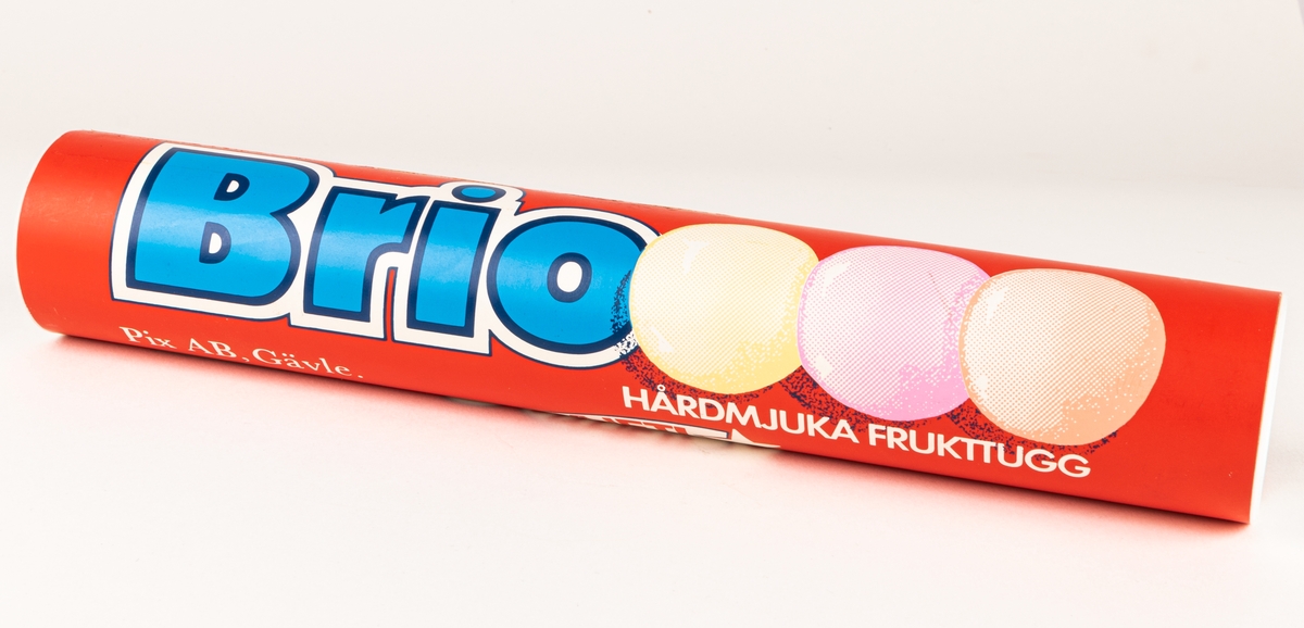 Pappersförpackning utan innehåll. Rör med vita plastlock i var ände. Text i blått och vitt. "BRIO, hårdmjuka frukttugg, Nyhet!"