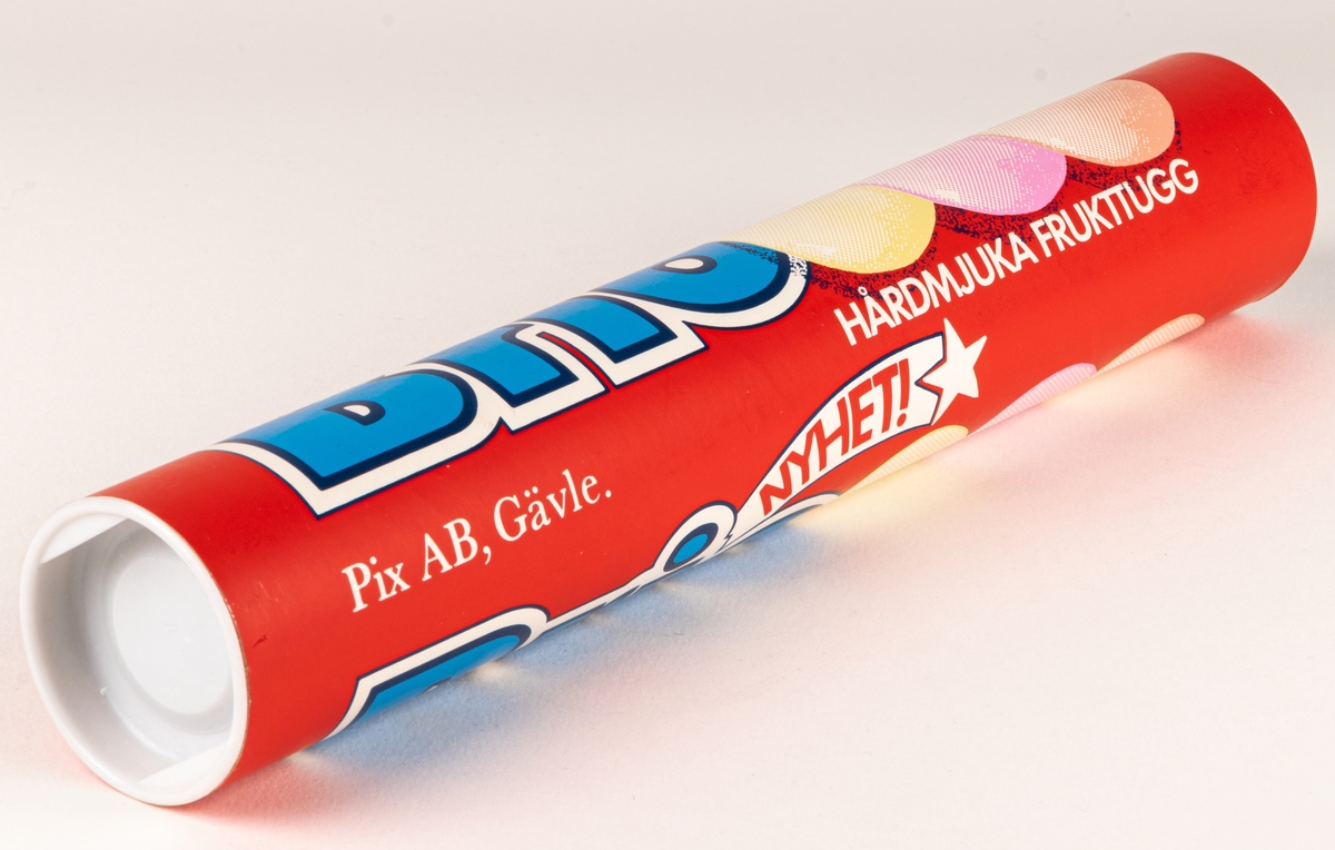 Pappersförpackning utan innehåll. Rör med vita plastlock i var ände. Text i blått och vitt. "BRIO, hårdmjuka frukttugg, Nyhet!"