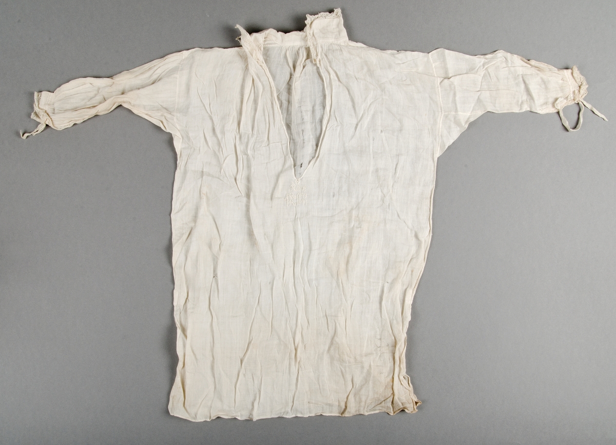 Skjorta för barn. Vit bomullslärft. Långa ärmar med trekantskil. Vit spets på kragen och vid handlederna. Sprund framtill utan knapper. Små knytband av vitt siden vid handlederna. Nedanför sprundet broderat i vitt initialer och årtal: R 1808, IAR 1844 P-R 1847.
Små hål här och var på både framsidan , ärmarna och baksidan. tyget är mer trasigt på skjortans baksida. Stort hål under högra ärmen. Fläckar på baksidan upptill, framsidan nedtill m.m.