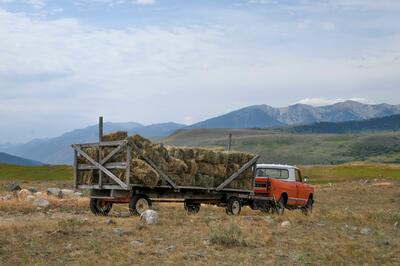 rød gammel pickup med stor tilhenger med firkantede høyballer i amerikansk storslagent landskap og fjell