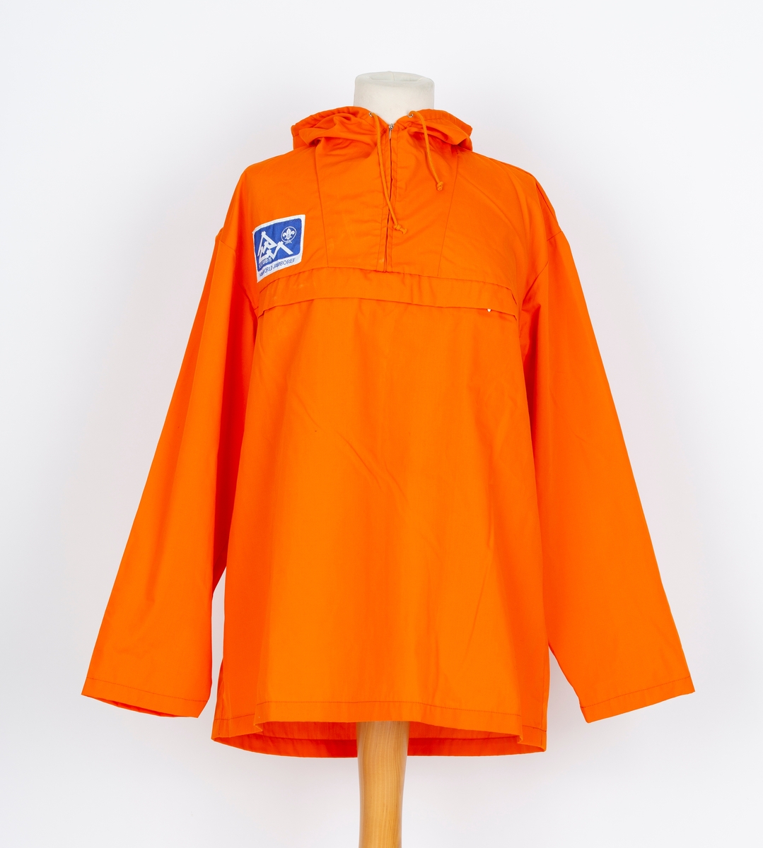 Anorakk. Hette. Brystlomme. Påsydd blått og hvitt merke  merke: Norjamb 75 14. woeld jamboree. menber made of Swiss Polyester
Givers ektemann Per Ottesen var disponent for Speidersport og hadde leveranser av utstyr og merkeklær til deltakere på leiren