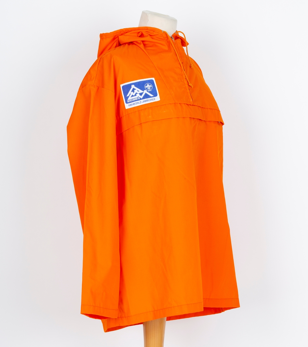 Anorakk. Hette. Brystlomme. Påsydd blått og hvitt merke  merke: Norjamb 75 14. woeld jamboree. menber made of Swiss Polyester
Givers ektemann Per Ottesen var disponent for Speidersport og hadde leveranser av utstyr og merkeklær til deltakere på leiren