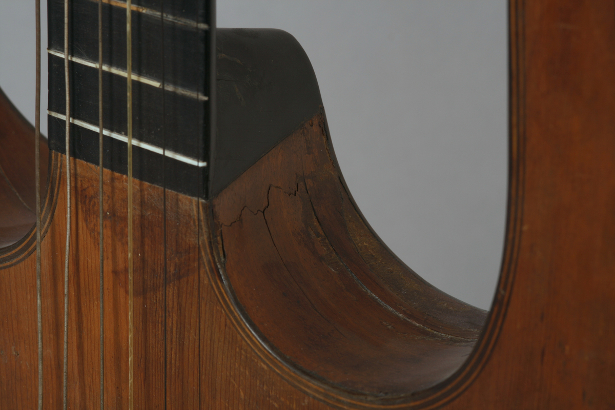 Vanlig gitar i omtrentlig gresk lyreform: korpus, gripebrett og to armer i et stykke. Armene forbundet øverst, gjennom skruekassen, ved et åk av metall. 6 strenger.

Stemmeskruer av ibenholt med perlemorsøye. Skruene festet undenifra. 13 bånd: 4 av ben, 9 av tre. 2 lydhull i form av gjennombrutte rosetter. Hals, gripebrett, strengefestet, fotstykke og kant rundt lydhullene av ibenholt. Knapper til strengefest av ibenholt med perlemor innlegg. Lokk av gran, sider og bunn mahogny. 
På innsiden av korpus to ribber av nåletre på tvers over bunn helt fram til sargene. 1 ribbe på tvers under lokk ovenfor rosettene.

Stil: Empire.