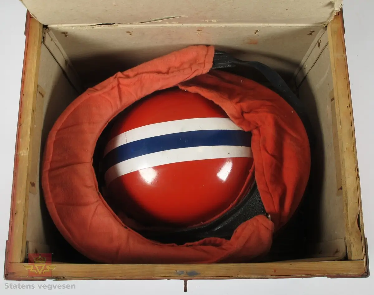 Hjelm med norsk profilering som består av flere lag/skall. De ytterste lagene er laget av tre og innsiden er laget av kork. Det er lagt skinn og tekstil som en myk barriere mellom hjelmen og hode. Med hjelmen tilhører det 2. stk. Visir laget av skinn og plast som er pakket inn i stoff for beskyttelse. Det hele er lagret i en medfølgende rød eske laget av tre og papp på innsiden.