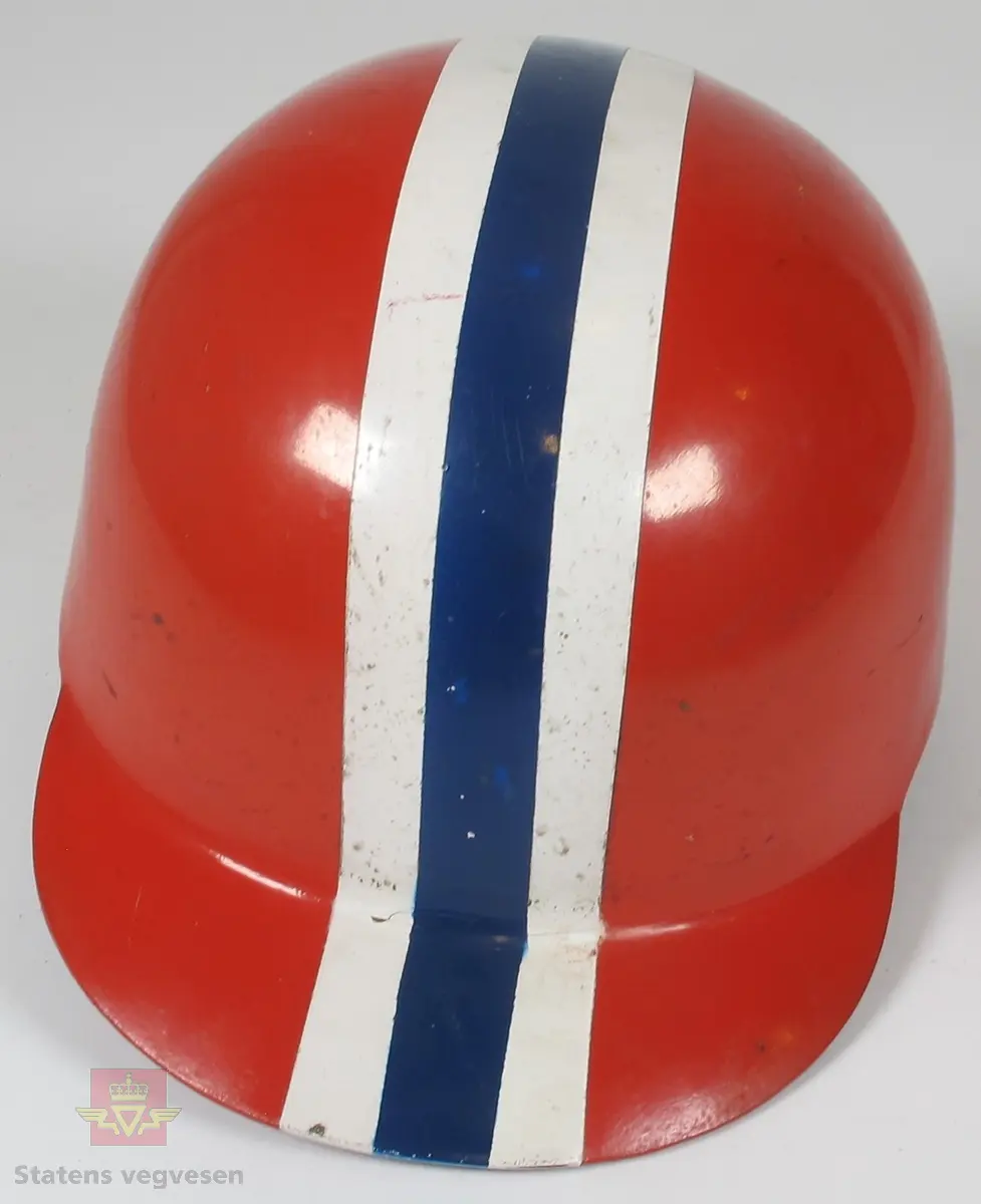Hjelm med norsk profilering som består av flere lag/skall. De ytterste lagene er laget av tre og innsiden er laget av kork. Det er lagt skinn og tekstil som en myk barriere mellom hjelmen og hode. Med hjelmen tilhører det 2. stk. Visir laget av skinn og plast som er pakket inn i stoff for beskyttelse. Det hele er lagret i en medfølgende rød eske laget av tre og papp på innsiden.