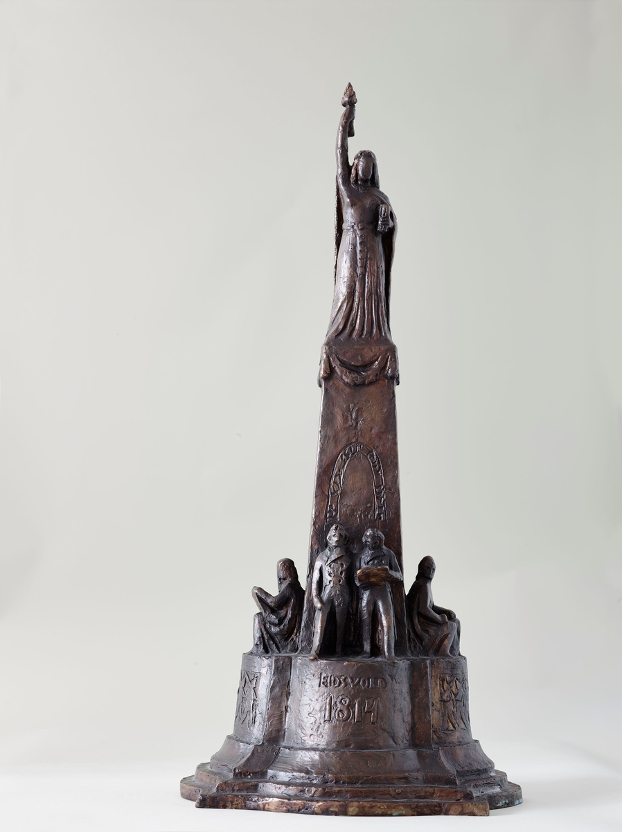 Støypt etter ASM 188 i gips som er eit utkast til toppfigur til Eidsvoldsøyle. Frå omkring 1905 var Svor mykje oppteken med planar om å pryde Eidsvolds plass i Kristiania, der Eidsvoldsmonumentet skulle reisast. Han tenkte seg ei fontene som skulle slutte seg til monumentet både i stil og tanke. Han såg frigjeringsverket på Eidsvoll som eit fornyande kjeldesprang, såvel for landet sitt åndelege som materielle liv.