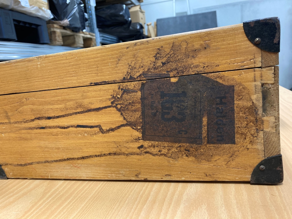 Trekoffert med hengslet lokk. Laget av plater, planker og lister. Metallbeslag i hjørnene. Håndtak på langsiden med vedheftet treskilt merket "8218" på fremsiden og på baksiden J. Østlie. Papiretikett på kortsiden "Halden 183". Kassen inneholder fangedrakten til Johan Østlie, Kornsjø, brukt i Grini fangeleir.