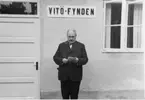 Grenna Hembygdsförenings ordförande A E Bolling talar i samband med Vitömuseets invigning. Han står framför en putsad byggnad med en skylt på väggen med texten 