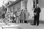 En man med hatt i händerna håller ett tal framför Vättermuseet i samband med dess invigning. Till vänster står manskören Sångarbröderna.