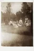 En familj sitter på gräsmattan i en trädgård. 1910-tal.