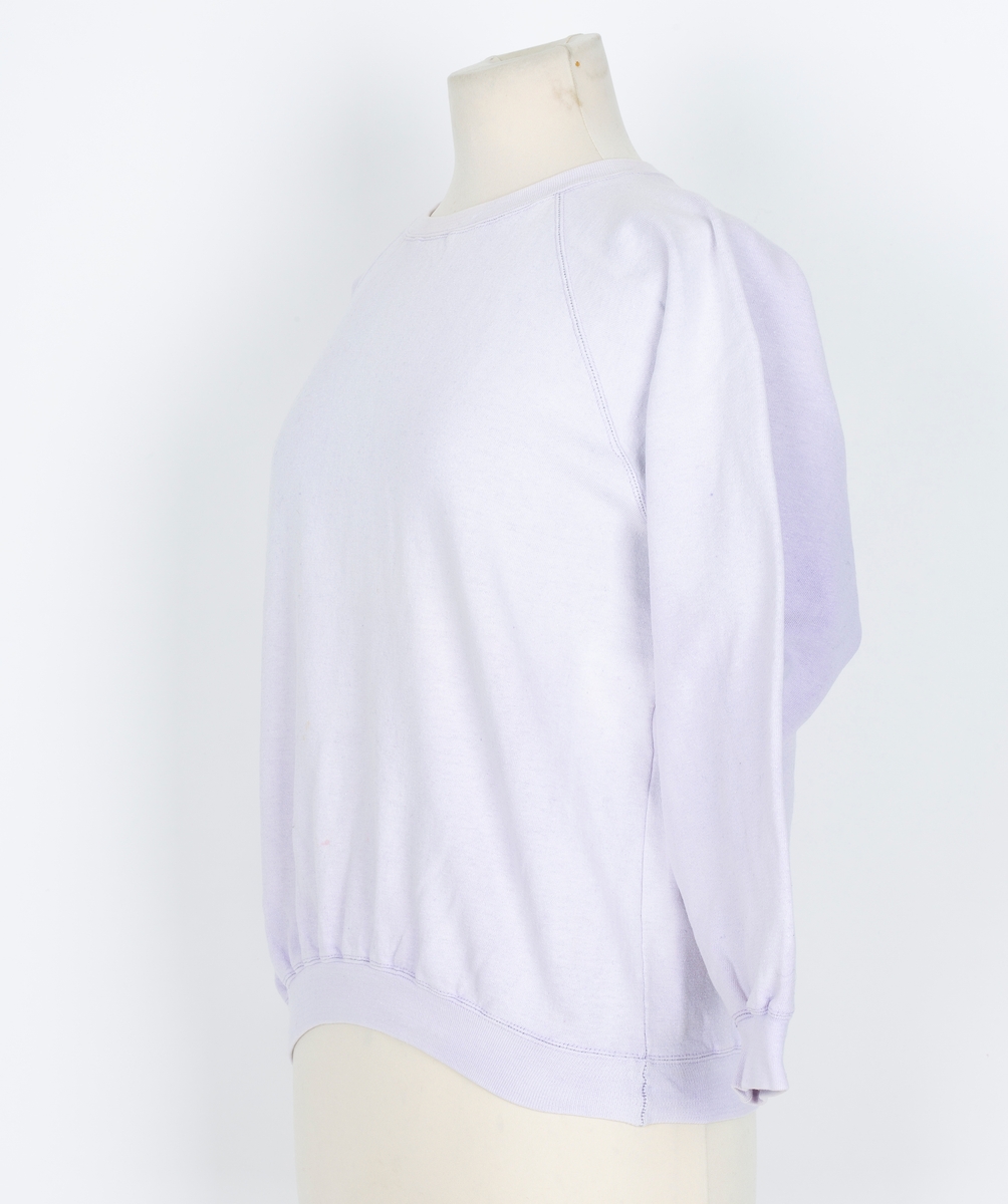 Joggedress. Todelt. Tricot. Lys lilla. Genser med raglan ermer, vrangborder. Bukse med strikk i livet, vrangbord på bukseben.
Brukt til uke-trim og fritid sent 1980-tall
