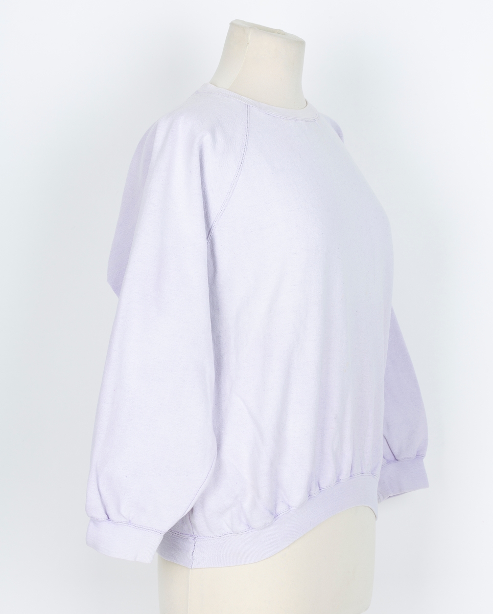 Joggedress. Todelt. Tricot. Lys lilla. Genser med raglan ermer, vrangborder. Bukse med strikk i livet, vrangbord på bukseben.
Brukt til uke-trim og fritid sent 1980-tall
