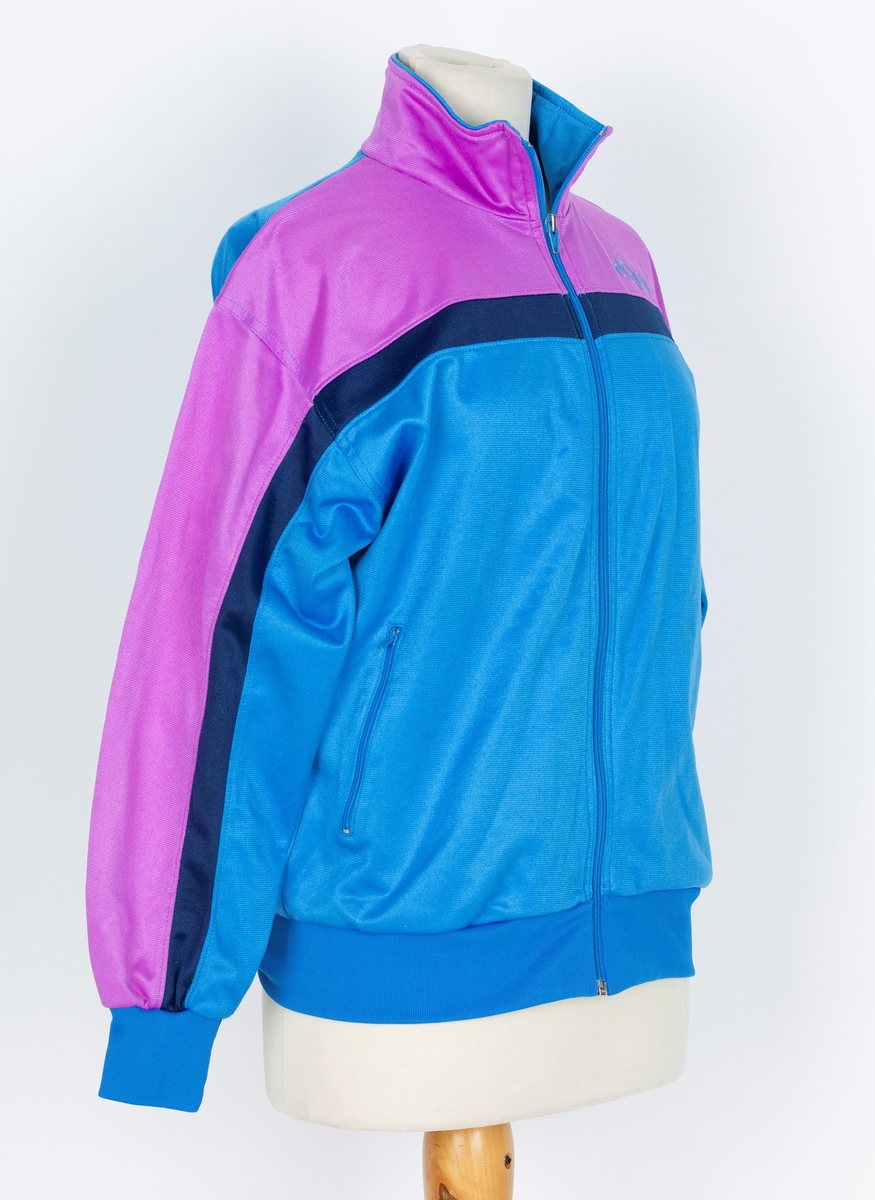 Joggedress. Lilla øverst, mørk blå stripe, blåturkis nederst.
A: jakke: Glidelås foran. Ståkrage.  
B: Bukse. Snor i livet, trikotmansjett nederst. mørk blå stripe i siden.

Kjøpt hos Wistex, Vestby.
Brukt undere sykehusopphold 1990 tallet. godt likt og mye brukt
