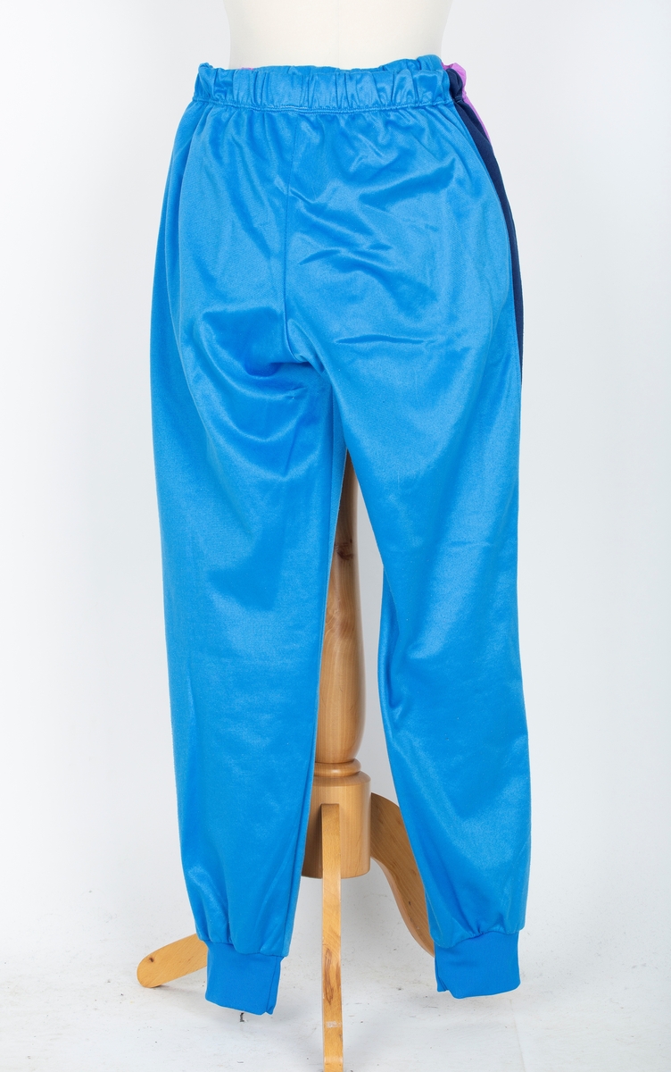 Joggedress. Lilla øverst, mørk blå stripe, blåturkis nederst.
A: jakke: Glidelås foran. Ståkrage.  
B: Bukse. Snor i livet, trikotmansjett nederst. mørk blå stripe i siden.

Kjøpt hos Wistex, Vestby.
Brukt undere sykehusopphold 1990 tallet. godt likt og mye brukt