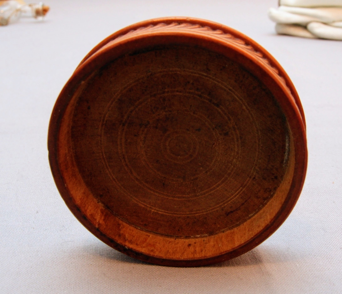 Svarvad rund ask i lackat trä. Med snidad dekor som täcker askens alla delar. Asken öppnas genom att ”delas” på mitten (består av två halvor som sammanfogas).  På askens ovansida föreställer dekoren ett fält där ändarna avslutas med bladdekor. I fältet är namnet ”Tilda” inristat. Bakom detta fält finns mer dekor föreställande blad. Dekoren på askens sidor består av lutande streck (som går i olika riktningar på de olika halvorna av asken). Asken har en rund yta med en svårtydd text i botten.