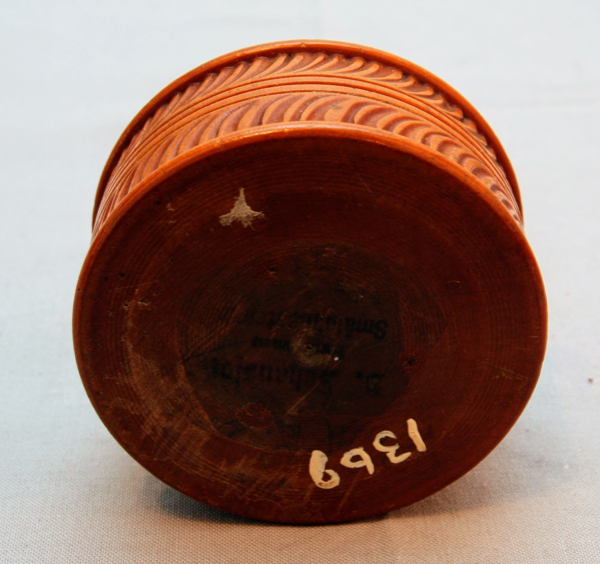 Svarvad rund ask i lackat trä. Med snidad dekor som täcker askens alla delar. Asken öppnas genom att ”delas” på mitten (består av två halvor som sammanfogas).  På askens ovansida föreställer dekoren ett fält där ändarna avslutas med bladdekor. I fältet är namnet ”Tilda” inristat. Bakom detta fält finns mer dekor föreställande blad. Dekoren på askens sidor består av lutande streck (som går i olika riktningar på de olika halvorna av asken). Asken har en rund yta med en svårtydd text i botten.