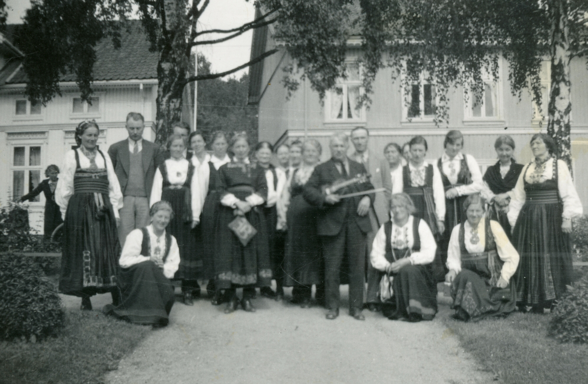 Gruppe med folkedrakter framfor hus