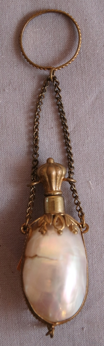 Luktdosa gjord av pärlemoskimrande, ovala snäckskal som hålls samman av en smal ornerad mässingsskena i form av pärlstav. Upptill avslutas dosan av en hals (i formpressad metall i form av blad och bär) i vilken det sitter en kork med ett hölje i mässing. Dosan hänger i en kedja som är fäst i två ringar på sidan av korken och som avslutas med en ring som är dekorerad med en pärlstav. På botten av dosan hänger ett litet droppformat avslut i metallskenan.