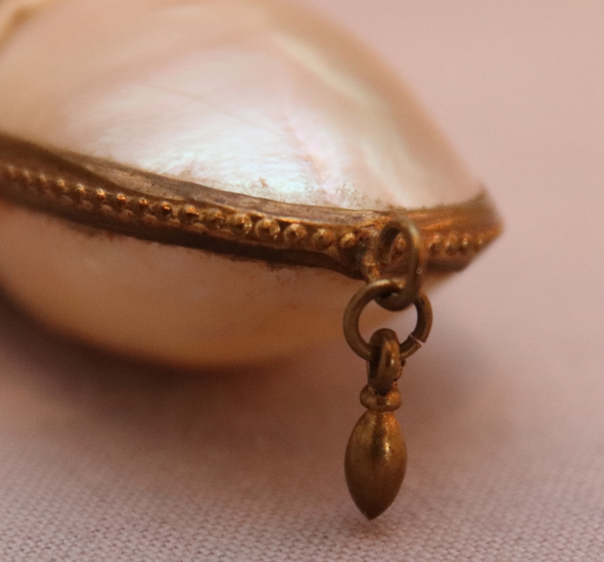 Luktdosa gjord av pärlemoskimrande, ovala snäckskal som hålls samman av en smal ornerad mässingsskena i form av pärlstav. Upptill avslutas dosan av en hals (i formpressad metall i form av blad och bär) i vilken det sitter en kork med ett hölje i mässing. Dosan hänger i en kedja som är fäst i två ringar på sidan av korken och som avslutas med en ring som är dekorerad med en pärlstav. På botten av dosan hänger ett litet droppformat avslut i metallskenan.