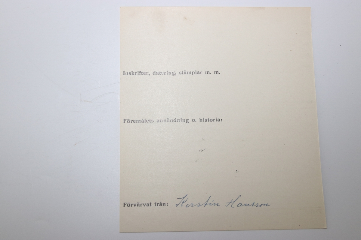 Luktdosa gjord av pärlemoskimrande, ovala snäckskal som hålls samman av en smal ornerad mässingsskena i form av pärlstav. Upptill avslutas dosan av en hals (i formpressad metall i form av blad och bär) i vilken det sitter en kork med ett hölje i mässing. Dosan hänger i en kedja som är fäst i två ringar på sidan av korken och som avslutas med en ring som är dekorerad med en pärlstav. På botten av dosan hänger ett litet droppformat avslut i metallskenan.